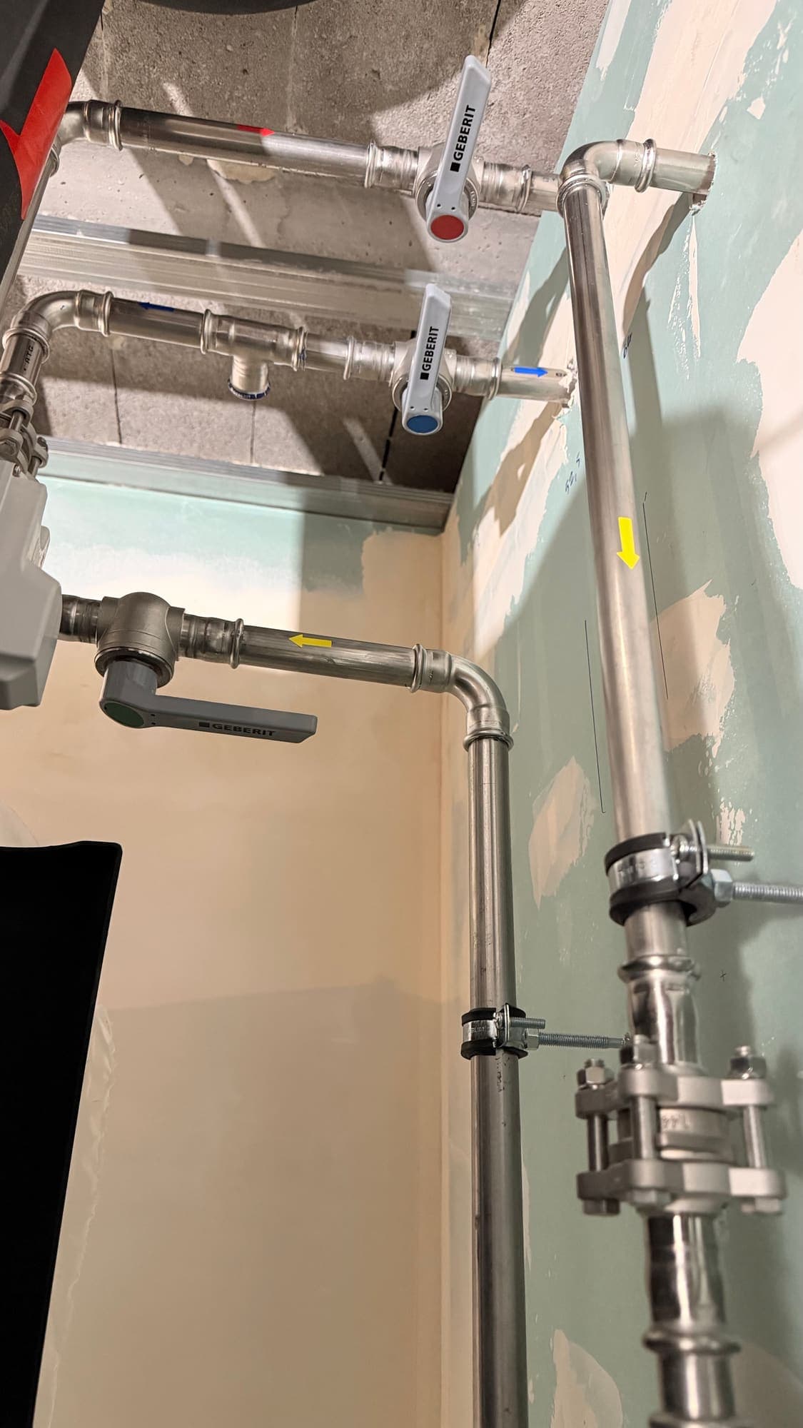 Geberit isolation valves with red and blue handles on stainless steel pipes, with flow direction arrows
