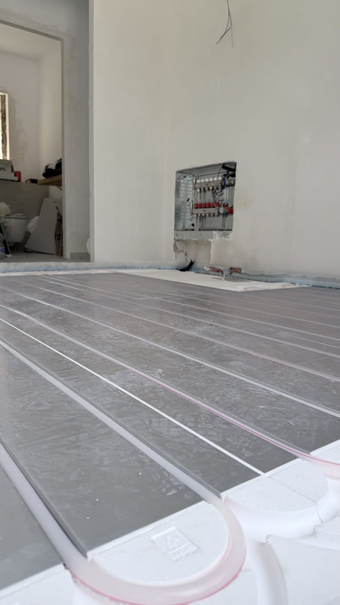 Low-inertia underfloor heating system with metal diffuser plates and the manifold in the background