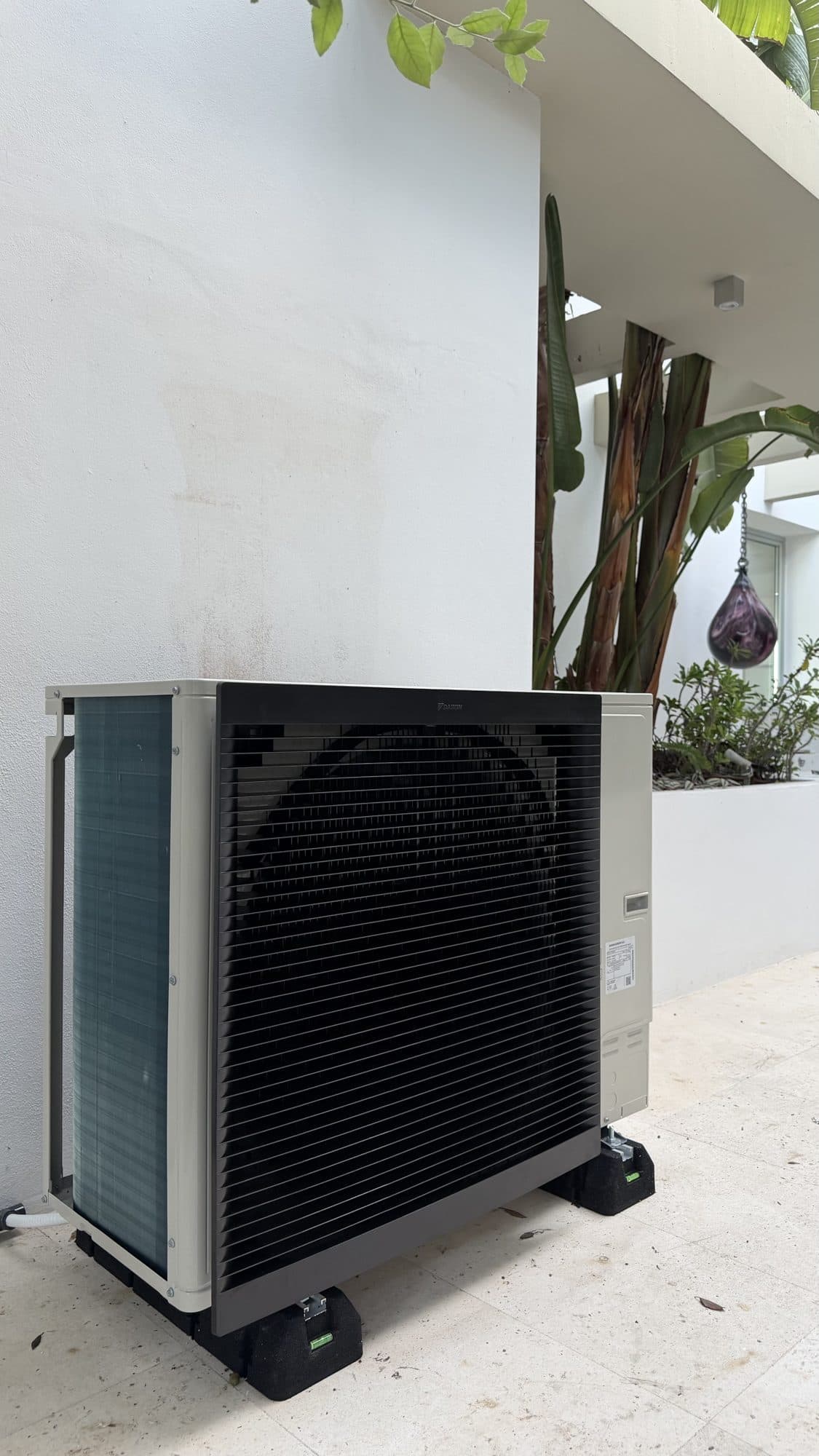 Unidad exterior de una bomba de calor aire-agua bibloc, sobre soportes antivibratorios en el patio de una vivienda